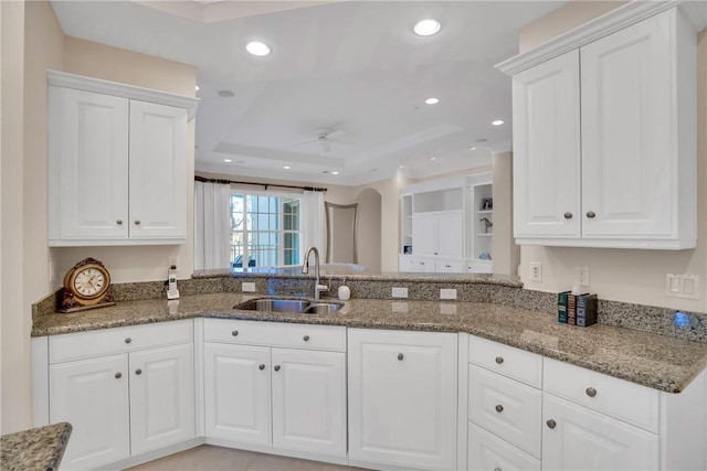 kitchen featuring stone counters, a tray ceiling, a sink, and recessed lighting