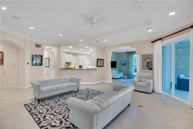 living area featuring arched walkways, a raised ceiling, light tile patterned flooring, and recessed lighting