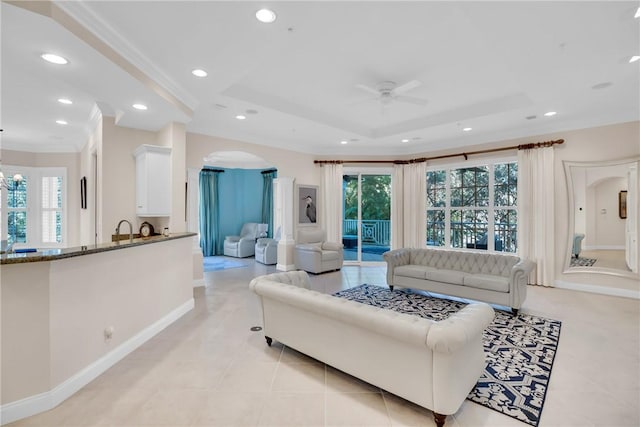 living room featuring arched walkways, recessed lighting, a raised ceiling, ornamental molding, and ceiling fan with notable chandelier