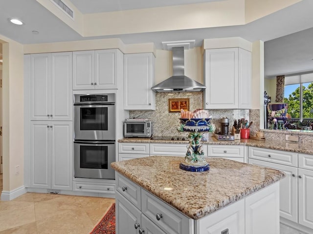 kitchen with wall chimney exhaust hood, double oven, recessed lighting, light stone counters, and decorative backsplash