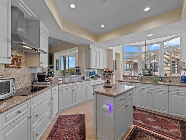 kitchen with black electric stovetop, wall chimney range hood, white cabinetry, decorative backsplash, and a sink