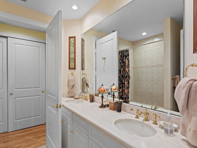 bathroom featuring double vanity, a tile shower, a sink, and wood finished floors