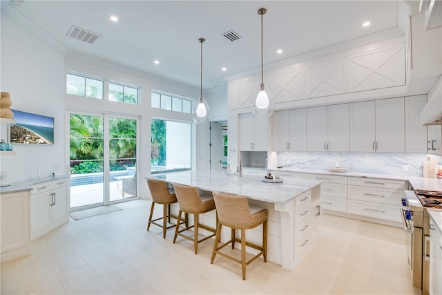 kitchen with high end stainless steel range oven, light stone counters, decorative backsplash, an island with sink, and ornamental molding