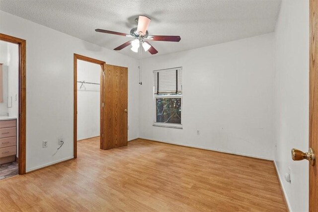 233 13th St SW, Vero Beach, FL 32962 - unfurnished bedroom featuring light wood-type flooring, a walk in closet, a closet, a textured ceiling, and ensuite bathroom