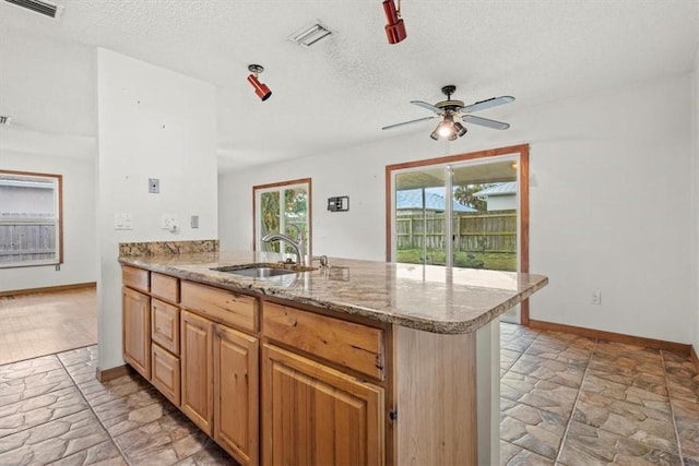 233 13th St SW, Vero Beach, FL 32962 - kitchen featuring a sink, light stone finish floors, a peninsula, a textured ceiling, and baseboards