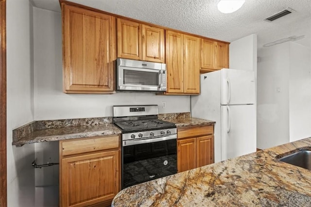 233 13th St SW, Vero Beach, FL 32962 - kitchen featuring stainless steel appliances, a textured ceiling, stone counters, and brown cabinetry
