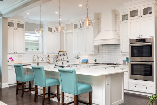 kitchen with crown molding, decorative backsplash, a center island with sink, custom range hood, and appliances with stainless steel finishes