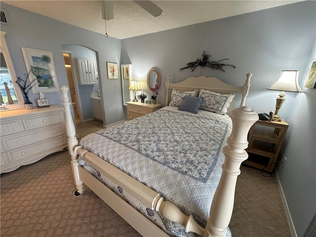 carpeted bedroom with a textured ceiling, ensuite bath, and ceiling fan