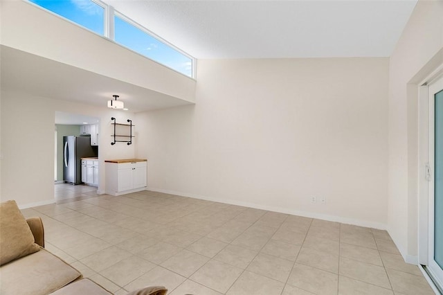 unfurnished living room with light tile patterned floors, a high ceiling, and baseboards