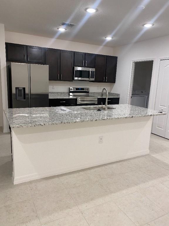 450 Hazel St, Sebastian, FL 32958 - kitchen with stainless steel appliances, an island with sink, light stone countertops, dark cabinets, and washer / clothes dryer