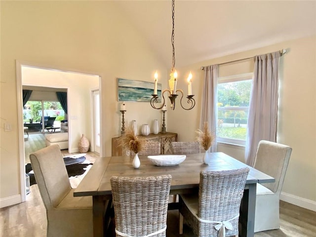 dining space with hardwood / wood-style flooring, a healthy amount of sunlight, high vaulted ceiling, and a notable chandelier