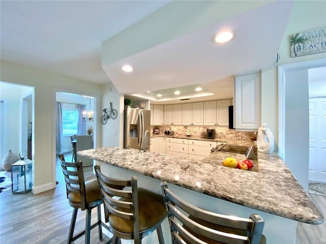 kitchen featuring stainless steel fridge with ice dispenser, white cabinets, a kitchen bar, decorative backsplash, and a tray ceiling