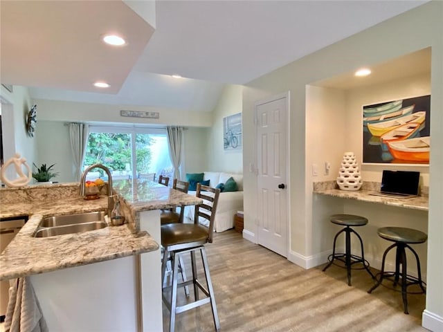 kitchen featuring a breakfast bar, sink, kitchen peninsula, and light wood-type flooring