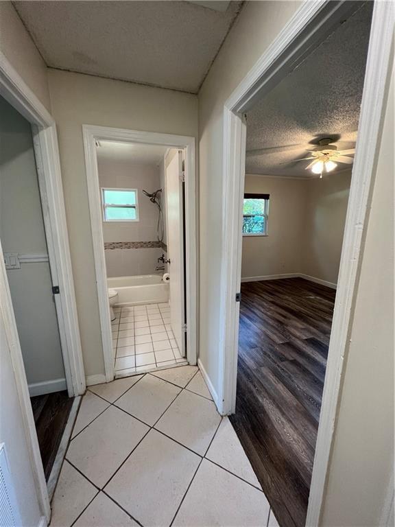 corridor featuring baseboards, light tile patterned flooring, and a textured ceiling
