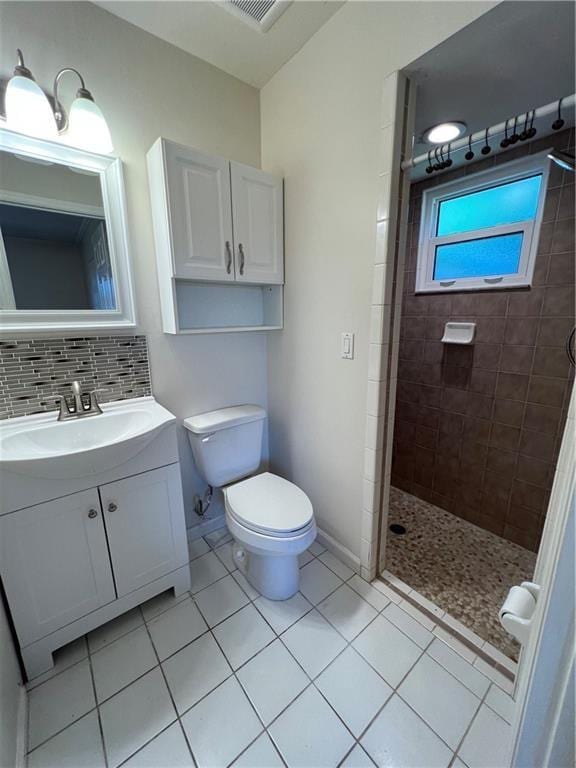 bathroom featuring a tile shower, vanity, toilet, tile patterned floors, and decorative backsplash