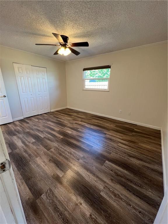 unfurnished bedroom with baseboards, a closet, a textured ceiling, and dark wood-type flooring
