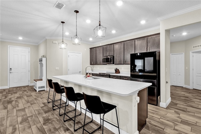 kitchen featuring dark brown cabinetry, sink, hanging light fixtures, a center island with sink, and stainless steel appliances