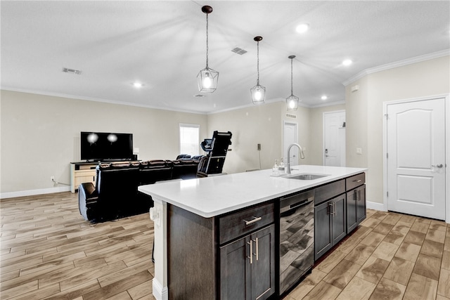 kitchen with sink, pendant lighting, ornamental molding, and an island with sink