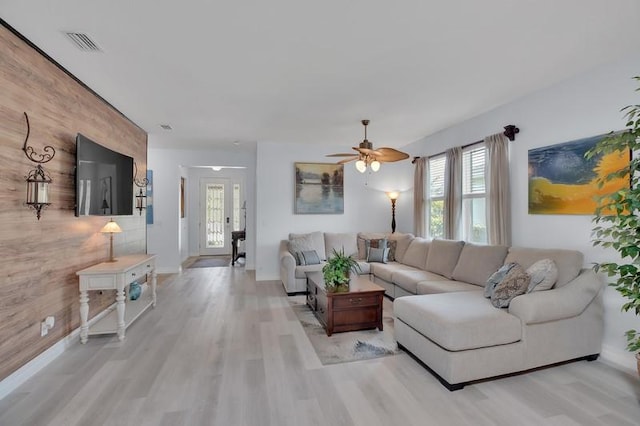 living area featuring visible vents, an accent wall, baseboards, light wood-type flooring, and a ceiling fan