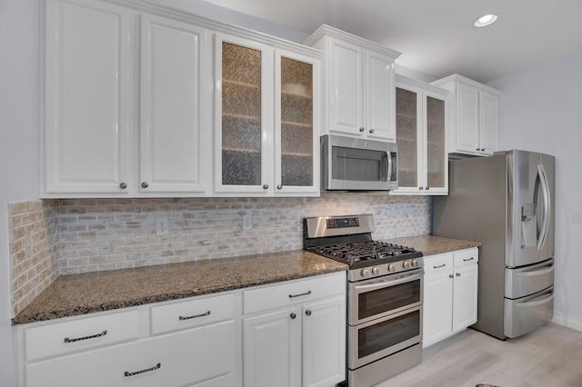 kitchen featuring decorative backsplash, appliances with stainless steel finishes, white cabinets, and dark stone counters