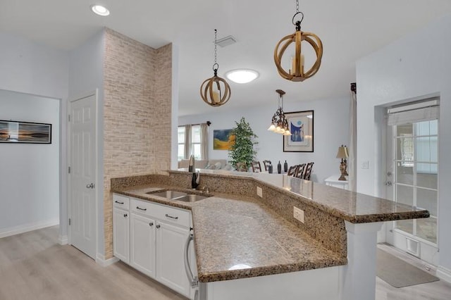 kitchen featuring a peninsula, dark stone counters, a sink, hanging light fixtures, and white cabinets