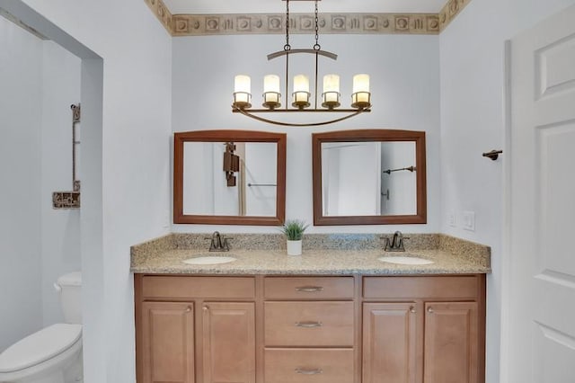 full bath featuring toilet, double vanity, a notable chandelier, and a sink