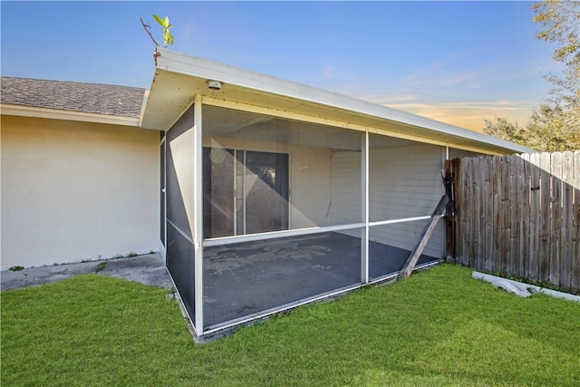 property exterior at dusk featuring a sunroom and a lawn