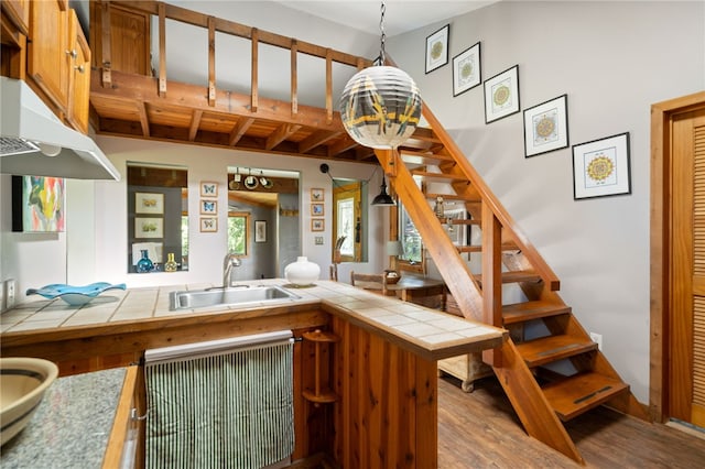 interior space with light wood-type flooring, sink, beam ceiling, tile counters, and hanging light fixtures