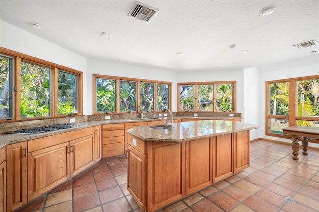 kitchen featuring light stone countertops, plenty of natural light, a center island with sink, and stainless steel gas stovetop