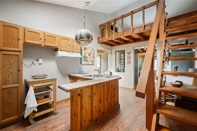 kitchen featuring kitchen peninsula, sink, wood-type flooring, tile counters, and hanging light fixtures