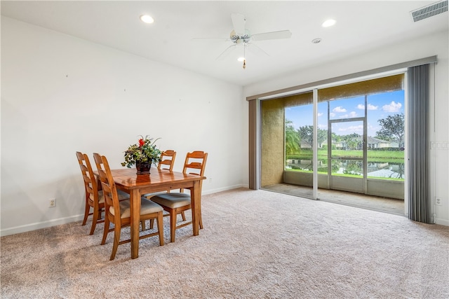 dining space with carpet floors, ceiling fan, and a water view