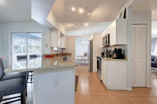 kitchen featuring light tile patterned floors, white cabinets, appliances with stainless steel finishes, and a peninsula