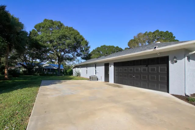 view of side of home with a lawn, cooling unit, stucco siding, a garage, and driveway