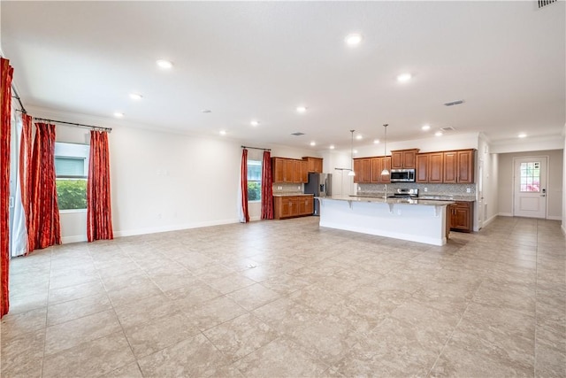 kitchen featuring stainless steel appliances, light stone counters, decorative backsplash, a breakfast bar, and a center island with sink