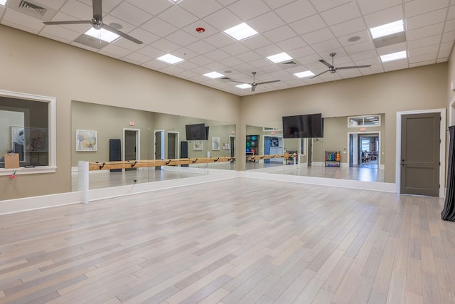 workout room featuring a drop ceiling, a towering ceiling, and light hardwood / wood-style floors