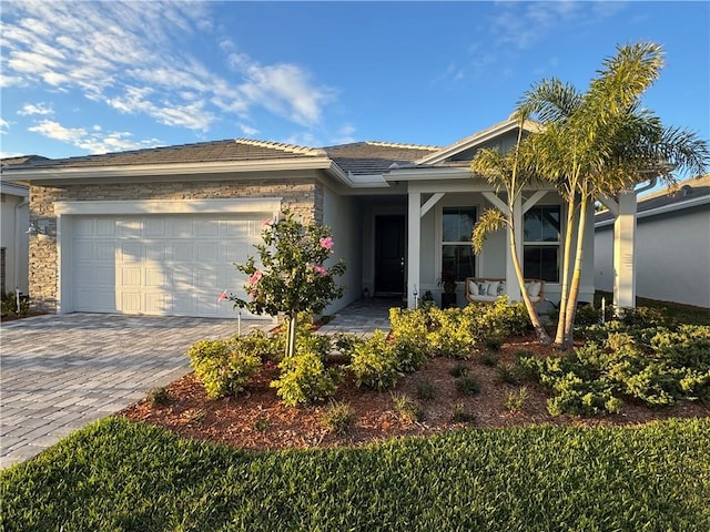 view of front of house featuring a garage, decorative driveway, covered porch, and stone siding