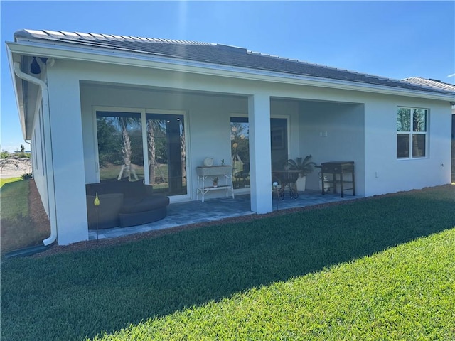 back of house featuring a lawn, a patio area, and stucco siding