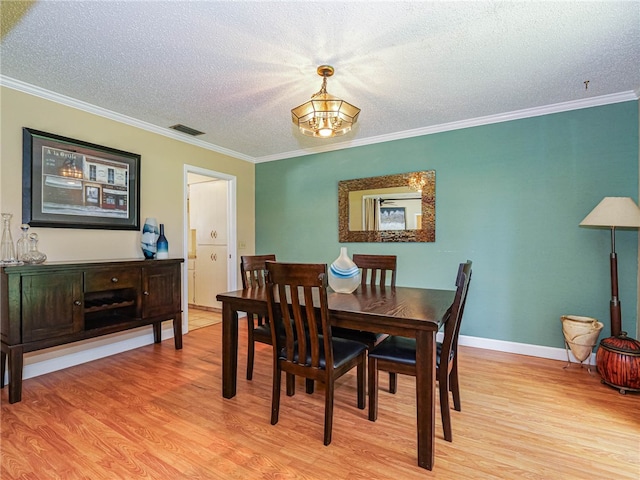 dining room featuring crown molding, light wood-type flooring, and a textured ceiling