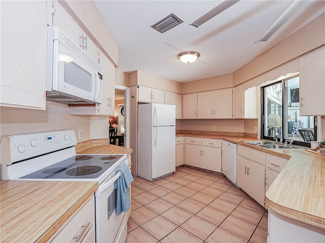 kitchen with white appliances, sink, a textured ceiling, light tile patterned flooring, and white cabinetry