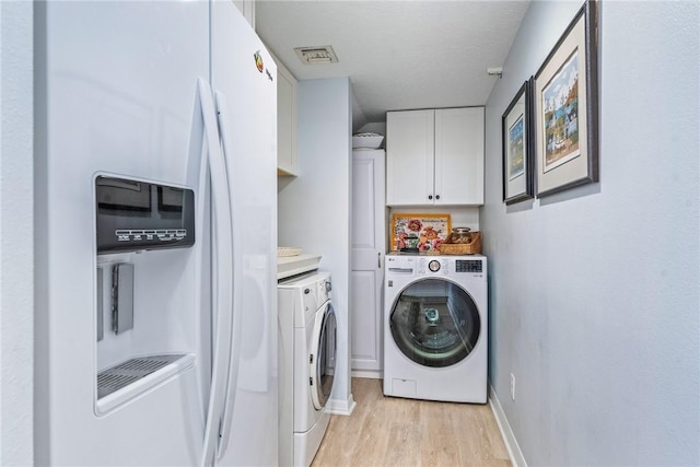 clothes washing area with cabinets, washing machine and dryer, and light hardwood / wood-style flooring