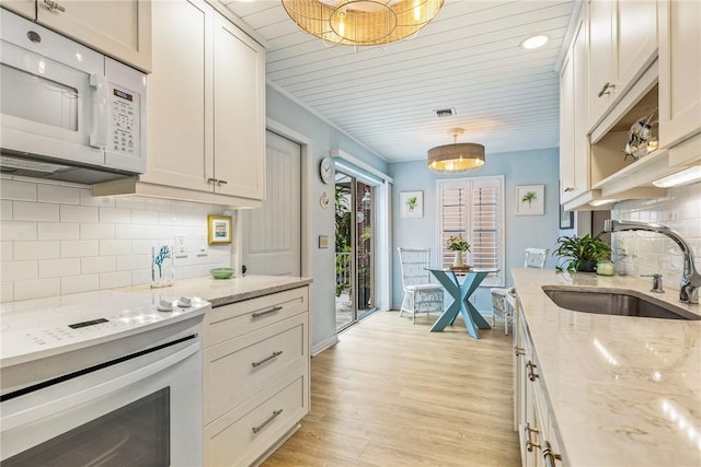 kitchen featuring decorative backsplash, light stone counters, sink, light hardwood / wood-style flooring, and hanging light fixtures