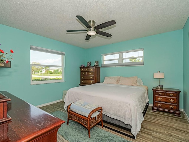 bedroom featuring a ceiling fan, multiple windows, baseboards, and wood finished floors