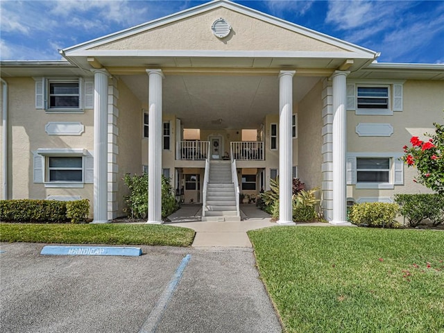 entrance to property featuring uncovered parking, a yard, and stucco siding