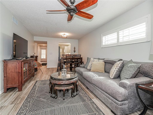 living area with visible vents, baseboards, ceiling fan, a textured ceiling, and light wood-style floors