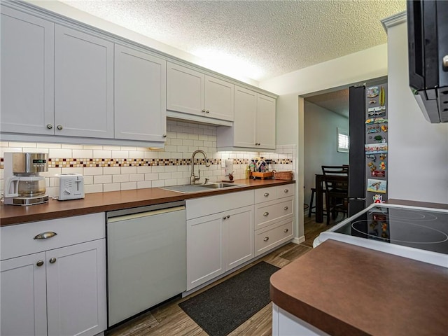 kitchen with wood finished floors, a sink, freestanding refrigerator, decorative backsplash, and dishwasher