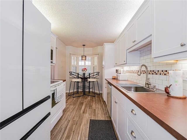 kitchen with light wood finished floors, decorative backsplash, white cabinets, a sink, and white appliances