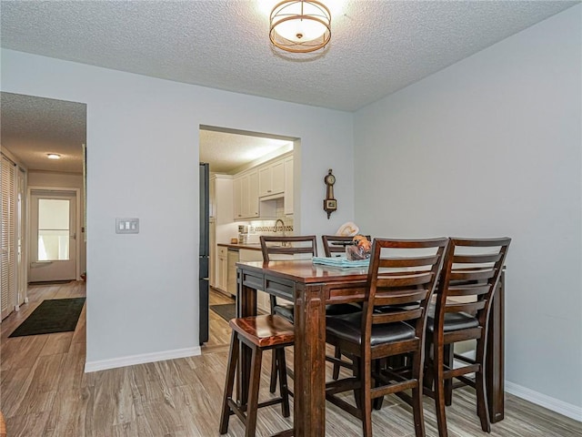 dining space featuring a textured ceiling, light wood finished floors, and baseboards