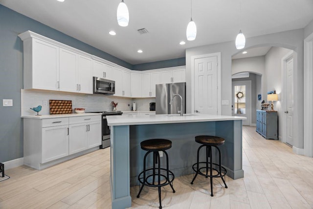 kitchen with white cabinetry, an island with sink, appliances with stainless steel finishes, backsplash, and pendant lighting