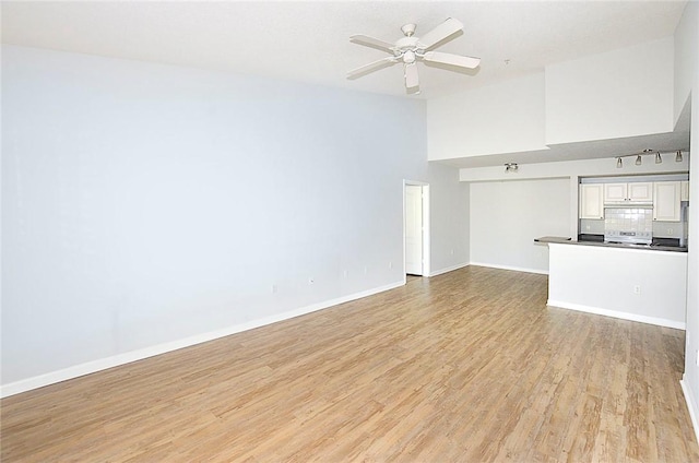 unfurnished living room featuring a high ceiling, ceiling fan, and light wood-type flooring