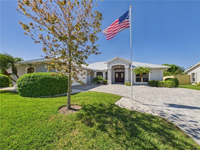 view of front of property with decorative driveway, fence, a front lawn, and stucco siding